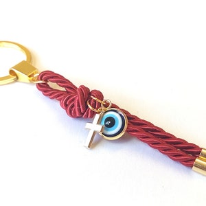 May include: Red rope keychain with a gold key ring, a gold cross charm, and a blue evil eye charm.