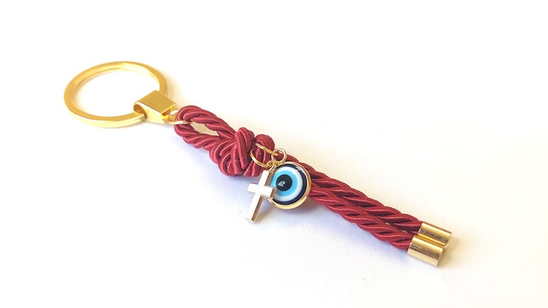 May include: Red rope keychain with a gold key ring, a gold cross charm, and a blue evil eye charm.