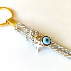 May include: A silver rope keychain with a gold ring, a gold cross charm, and a blue evil eye charm.