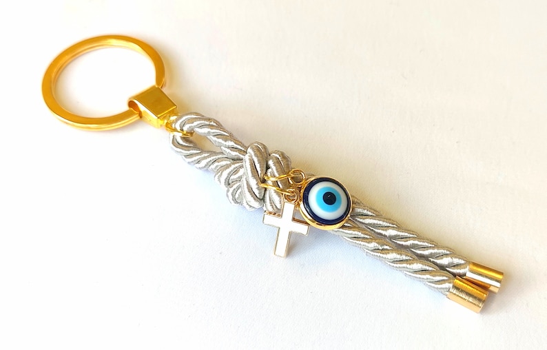 May include: A silver rope keychain with a gold ring, a gold cross charm, and a blue evil eye charm.