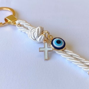 May include: White rope keychain with a gold key ring, a gold cross charm, and a blue evil eye charm.