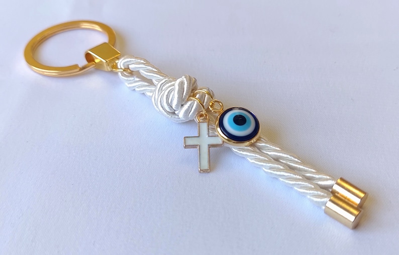 May include: White rope keychain with a gold key ring, a gold cross charm, and a blue evil eye charm.