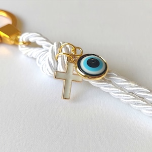 May include: White rope keychain with a gold key ring, a gold cross charm, and a blue and white evil eye charm.