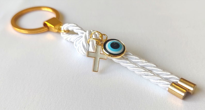 May include: White rope keychain with a gold key ring, a gold cross charm, and a blue and white evil eye charm.