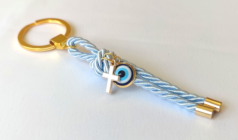 May include: A light blue braided keychain with a gold key ring, a gold cross charm, and a blue evil eye charm.