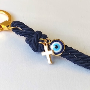 May include: A navy blue rope keychain with a gold key ring, a gold cross charm, and a blue evil eye charm.