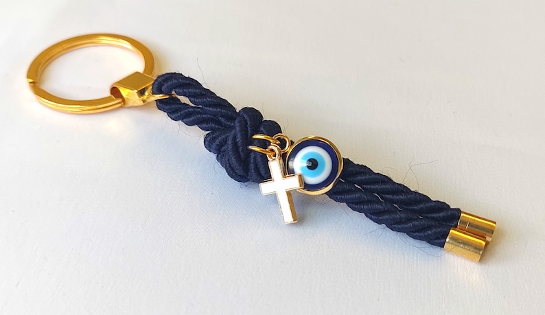 May include: A navy blue rope keychain with a gold key ring, a gold cross charm, and a blue evil eye charm.