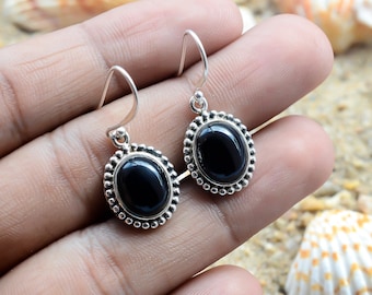 May include: A pair of silver earrings with black oval gemstones set in a beaded bezel. The earrings have a simple drop design.