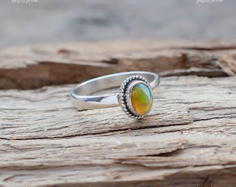 Può includere: Un anello d'argento con una pietra di opale ovale incastonata in una montatura d'argento. L'opale presenta una lucentezza iridescente verde e arancione.