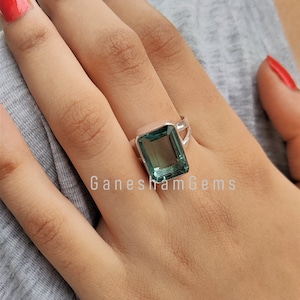 May include: A silver ring with a large, emerald green gemstone. The ring has a simple, elegant design and is set on a woman's finger.