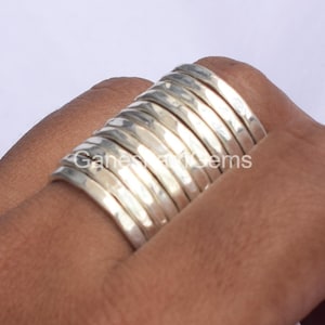 Puede incluir: Una pila de 12 anillos de plata martillados. Los anillos son todos del mismo tamaño y están apilados uno encima del otro.