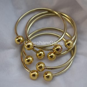 May include: Set of six gold-toned bangle bracelets with round ball accents. The bracelets are stacked on top of each other.