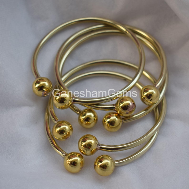 May include: Set of six gold-toned bangle bracelets with round ball accents. The bracelets are stacked on top of each other.