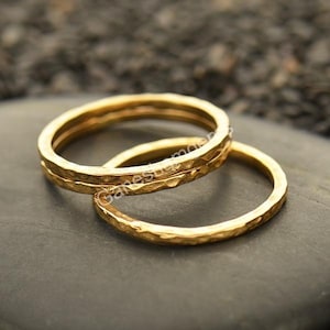 Könnte beinhalten: Zwei goldene, gehämmerte Ringe zum Stapeln. Die Ringe sind schlicht und zart, mit einer strukturierten Oberfläche.