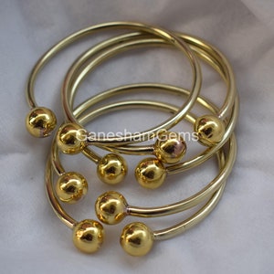 May include: Set of six gold-toned bangle bracelets with round ball accents. The bracelets are stacked on top of each other.