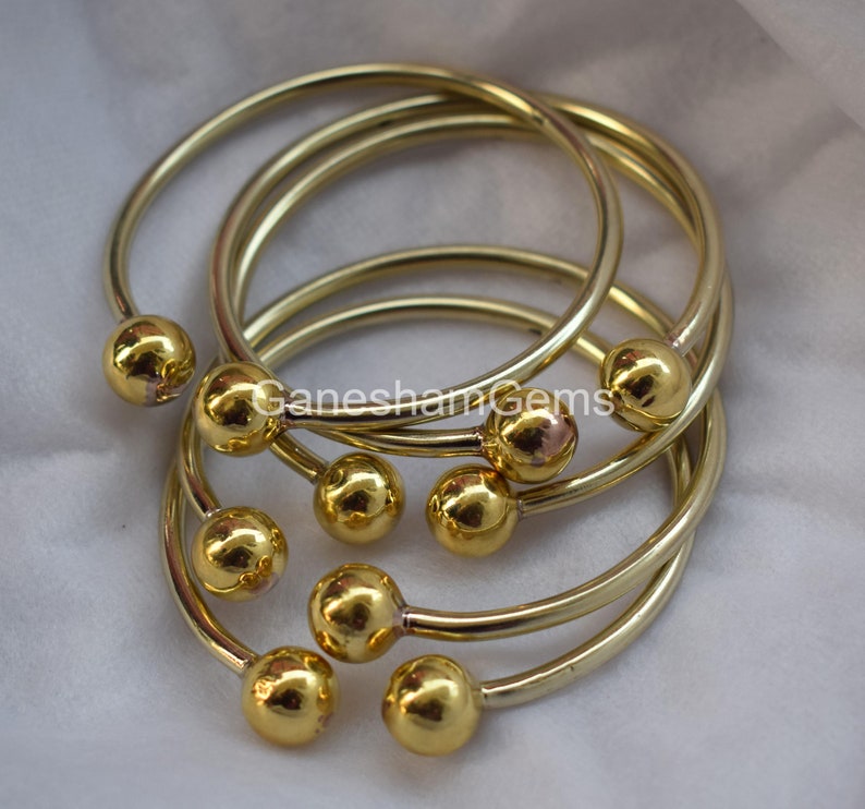 May include: Set of six gold-toned bangle bracelets with round ball accents. The bracelets are stacked on top of each other.