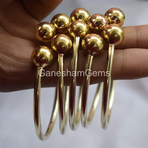 May include: Set of six gold-toned bangle bracelets with round ball accents. The bracelets are stacked on top of each other.