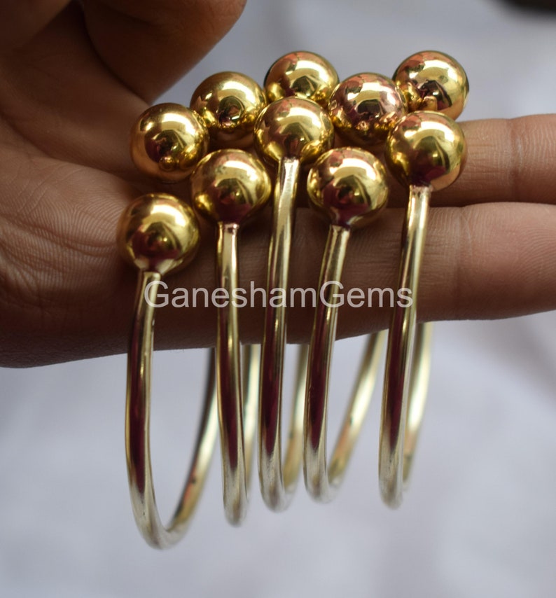 May include: Set of six gold-toned bangle bracelets with round ball accents. The bracelets are stacked on top of each other.