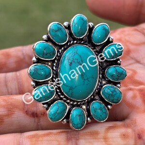 May include: A silver ring with a large turquoise stone surrounded by smaller turquoise stones. The ring has a floral design.