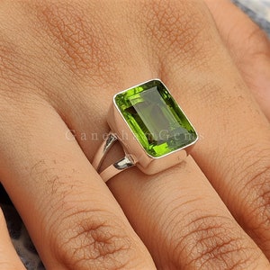 Puede incluir: Un anillo de plata con una gran piedra preciosa rectangular verde. El anillo tiene una caña dividida.