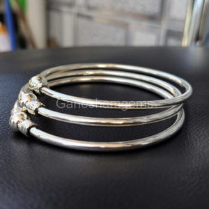 Peut inclure: Trois bracelets argent&eacute;s avec des ornements en forme de boules. Les bracelets sont circulaires et semblent &ecirc;tre en m&eacute;tal brillant. L'image est prise en gros plan, soulignant les d&eacute;tails des bijoux.