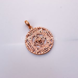 Puede incluir: Un colgante dorado con un diseño detallado e intrincado de un cuadrado dentro de un círculo. El colgante tiene un aspecto delicado y ornamentado, perfecto para agregar un toque de elegancia a cualquier colección de joyas.