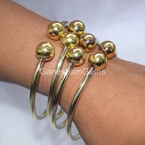 May include: Set of four gold bangle bracelets with round ball accents. The bracelets are stacked on a person's wrist.