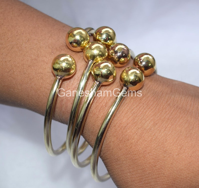 May include: Set of four gold bangle bracelets with round ball accents. The bracelets are stacked on a person's wrist.