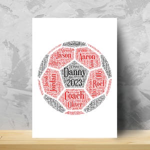 May include: A white poster featuring a soccer ball design made of names and soccer terms in black and red. The name "Danny" is prominently displayed in the center, with the year "2023" below it. Other names and terms are arranged to form the ball's pattern.