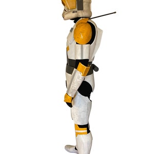 Op de afbeelding: Een volledig kostuum dat lijkt op een kloontrooper uit een sciencefictionfranchise. De bepantsering is voornamelijk wit met gele en grijze accenten. De helm heeft een kenmerkend ontwerp met een vizier en antenne. Het kostuum bevat een zwart onderpak en grijze laarzen.