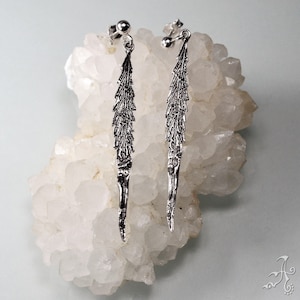 Op de afbeelding: Een paar zilveren oorhangers met een bladerenontwerp. De oorbellen hangen aan een witte kristallen cluster.