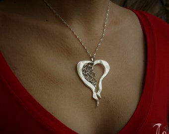 Op de afbeelding: Een zilveren ketting met een delicate, opengewerkte hart hanger. Het hart is ingewikkeld ontworpen met een filigraanpatroon en heeft een licht asymmetrische vorm.