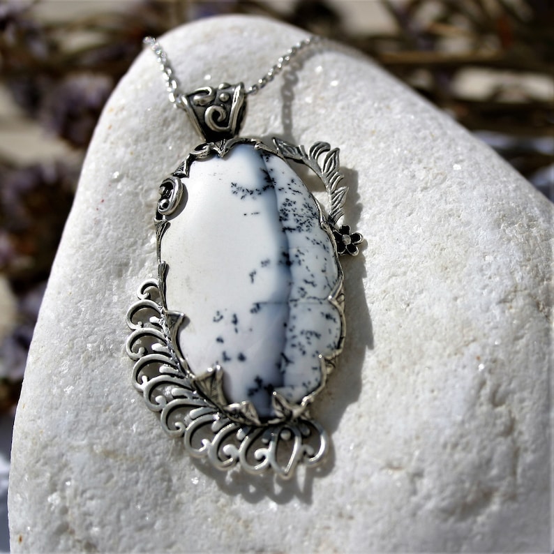 May include: A silver pendant necklace with a white and black dendritic agate stone set in a filigree design.