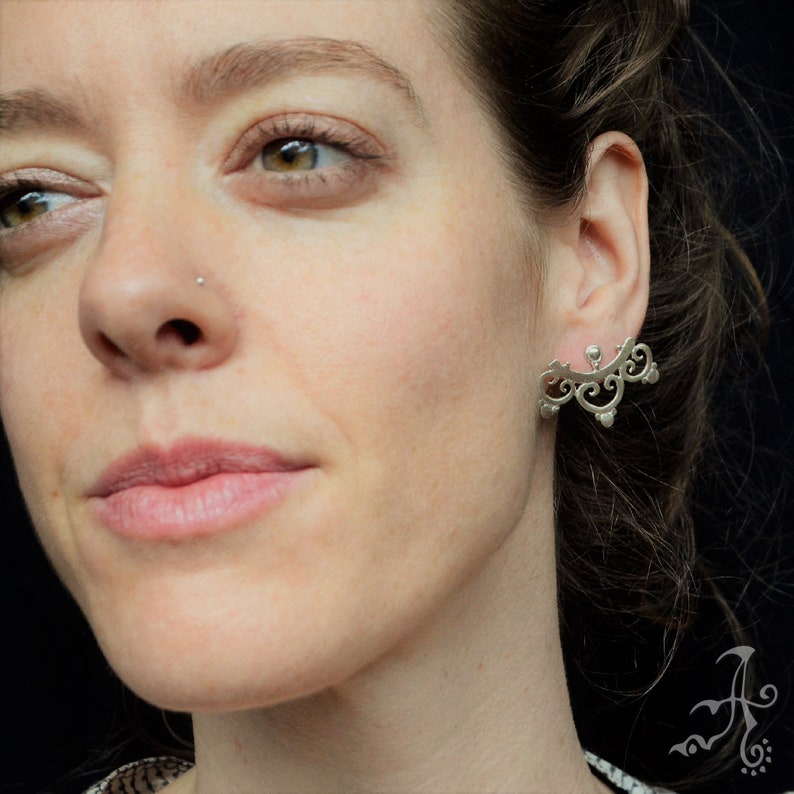 May include: Silver ear cuff with a delicate, intricate design. The cuff is shaped like a crescent moon and features a series of small, rounded details.