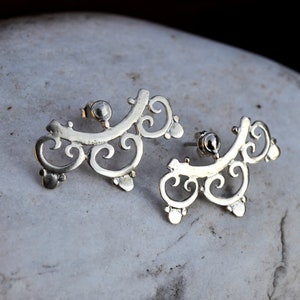 May include: A pair of silver earrings with a delicate, intricate design. The earrings are shaped like a series of swirls and curves, and they have a slightly curved shape.