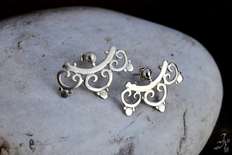 May include: A pair of silver earrings with a delicate, intricate design. The earrings are shaped like a series of swirls and curves, and they have a slightly curved shape.