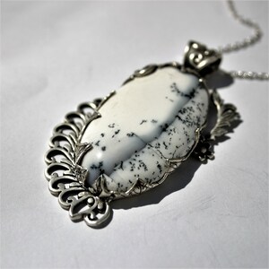 May include: A silver pendant necklace with a white and gray agate stone set in a filigree design.