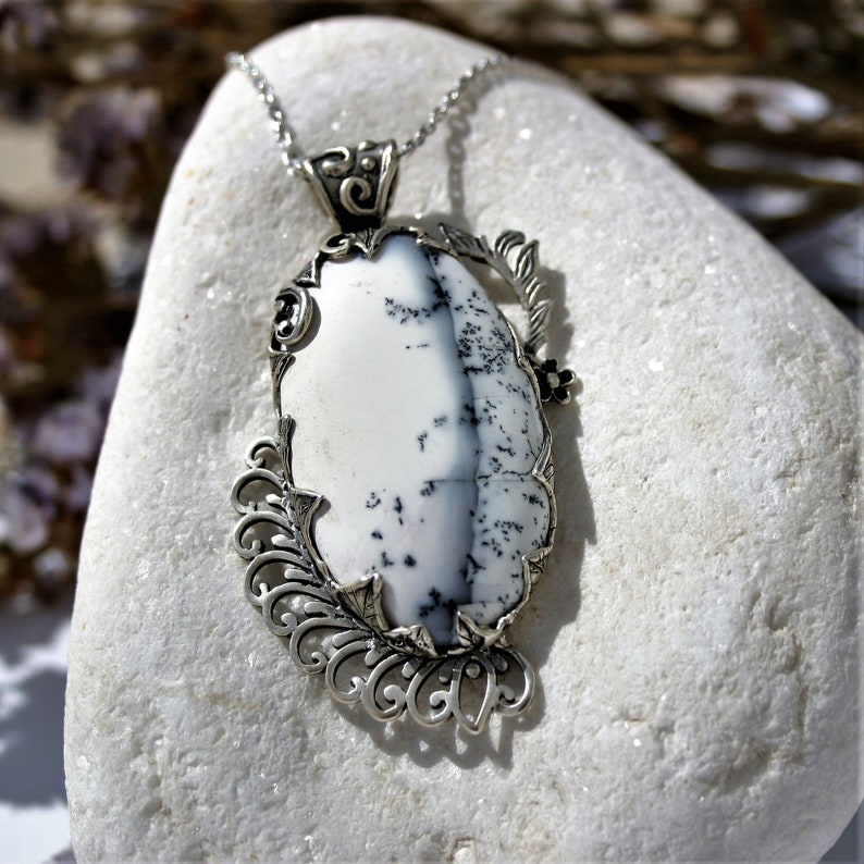 May include: A silver pendant necklace with a white and black dendritic agate stone set in a detailed filigree design.