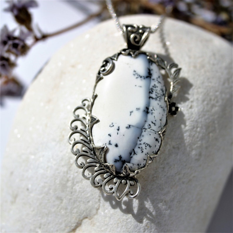 May include: A silver pendant with a white and black dendritic opal stone set in a filigree design.