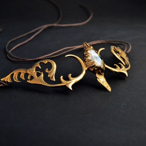 Pode incluir: Uma faixa de cabeça dourada com uma grande gema iridescente no centro. A faixa de cabeça tem a forma de chifres com detalhes intrincados.