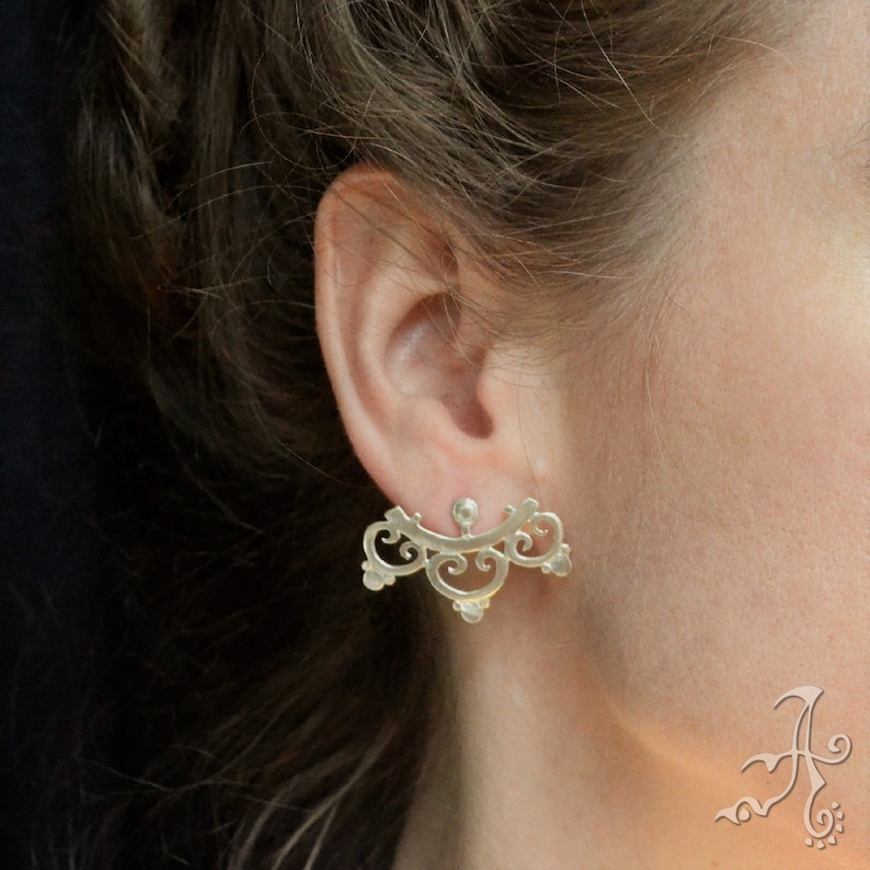 May include: Silver ear cuff earrings with a delicate, intricate design. The earrings are shaped like a fan and have a floral motif.