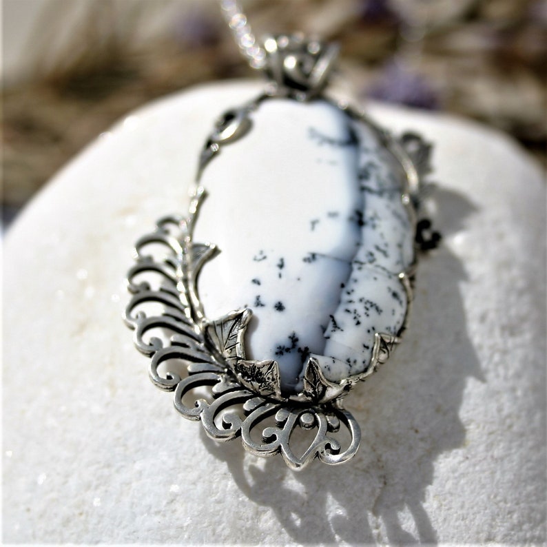 May include: A silver pendant with a white and black dendritic opal stone set in a delicate floral design.