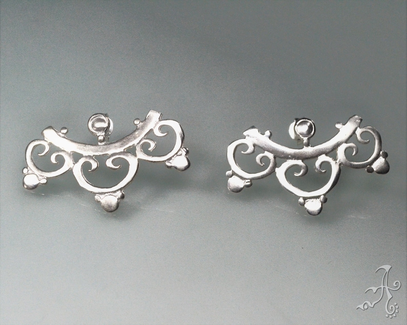 May include: A pair of silver filigree earrings with a delicate, intricate design. The earrings are shaped like a crescent moon with a small, round bead at the center.
