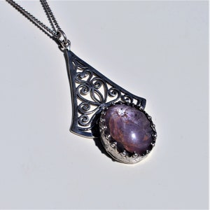 Peut inclure: Un collier avec un pendentif en argent, orné d'un motif de filigrane délicat et d'une grande pierre précieuse ovale de couleur violette.