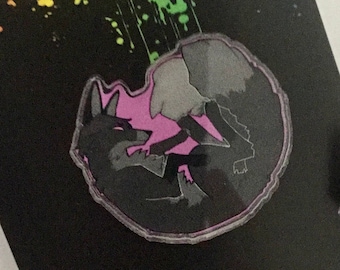 May include: Two black and gray enamel pins with a pink background. The pins depict two wolves facing each other with their heads tilted. The pins are on a black background with a rainbow splatter pattern.