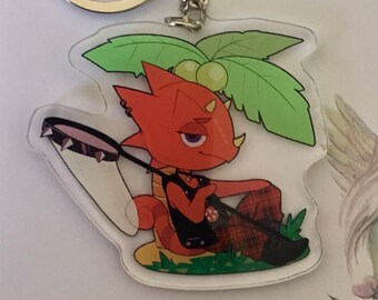 May include: A red and green cartoon character with a net sits on a green leaf with a yellow fruit. The character is a keychain with a silver ring.