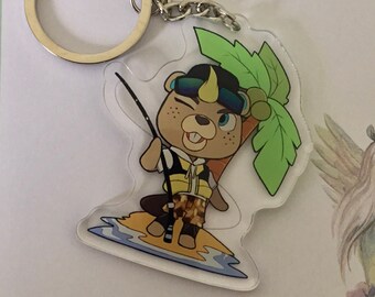 May include: A clear acrylic keychain featuring a cartoon beaver surfing on a wave. The beaver is wearing a yellow life vest and a black and yellow hat. The keychain has a silver metal ring.