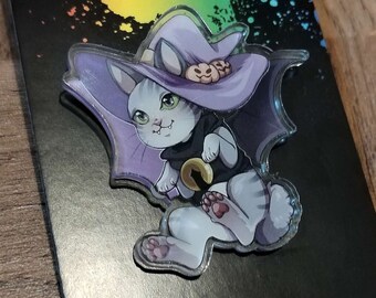 May include: A purple and white cat wearing a witch hat with a black cat on top. The cat is holding a bell in its paw. The background is black with rainbow paint splatters. The image includes the text "AZUWORKS".