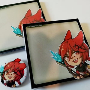 May include: Two black square boxes with a clear front panel and a red-haired anime character with blue eyes and a blue and gold staff. The character is wearing a red and black outfit. The boxes have the text "Graha Tia" printed on the front. A round button with the same character is also shown.