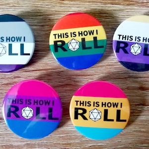 Peut inclure: Six boutons ronds avec différentes couleurs de drapeaux de fierté et un graphique de dé. Chaque bouton dit "This is how I roll".